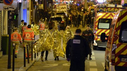 Des rescapés sous des couvertures de survie de l'attentat du Bataclan à Paris, le 13 novembre 2015, entourés par des secouristes. (MIGUEL MEDINA / AFP)