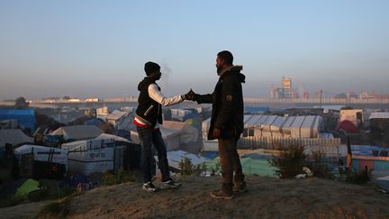 Deux hommes se saluent sur le point culminant du bidonville de réfugiés à Calais. (NEIL HALL / REUTERS)