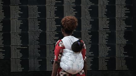 Une femme et son bébé devant le mur&nbsp;portant des noms de victimes du génocide du Rwanda, au mémorial de Kigali. (YASUYOSHI CHIBA / AFP)