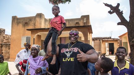 Dans la rue, les enfants n'hésitent pas à venir tâter les bras d'Iron Biby. Patient, ce colosse burkinabè d'1,90 mètre pour 180 kg et... 63 cm de tour de bras, star internationale des sports de force, laisse faire avec bienveillance.&nbsp; (OLYMPIA DE MAISMONT / AFP)