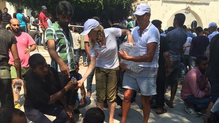 Des touristes hollandais distribuent des bouteilles d'eau aux migrants qui attendent devant le poste de police de Kos (Gr&egrave;ce), le 20 ao&ucirc;t 2015. (BENOIT ZAGDOUN / FRANCETV INFO)