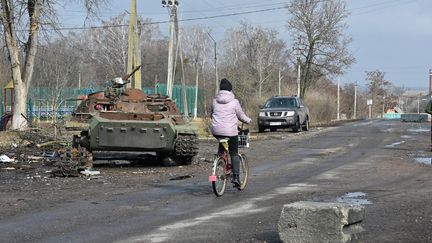 Une femme circule à vélo à Vovtchansk, près de Kharkiv (Ukraine), le 9 mars 2023. (SERGEY BOBOK / AFP)