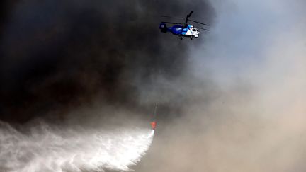 Un hélicoptère traverse un nuage de fumée émanant, des incendies de fôret, en repandant de l'eau pour tenter de l'éteindre, dans le district de Manavgat à Antalya, en Turquie, le 1er août 2021.&nbsp; (SULEYMAN ELCIN / ANADOLU AGENCY)