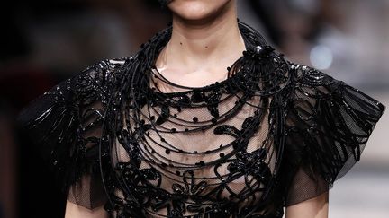 Chez Giorgio Armani Privé, les femmes avancent à petits pas dans leurs robes étroites scintillantes. Elles portent des petits chapeaux noirs à voilettes, une robe dont les broderies de perles bruissent, une jupe longue à sequins noirs, un haut entièrement couvert de plumes échancré dans le dos... Rose et noir dominent la palette de cette collection.
	 
 (Patrick KOVARIK / AFP)