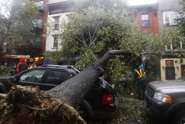 Un homme d&eacute;coupe un arbre tomb&eacute; sur une voiture &agrave; Hoboken (New Jersey), le 29 octobre 2012.&nbsp; (GARY ERSHORN / REUTERS )