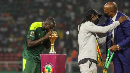 Le Sénégalais&nbsp;Kalidou Koulibaly (à gauche) embrasse la coupe pendant que son sélectionneur,&nbsp;Aliou Cissé, est félicité, après la victoire de l'équipe en finale de la Coupe d'Afrique des nations, le 6 février 2022, à Yaoundé (Cameroun) (AYMAN AREF / NURPHOTO / AFP)