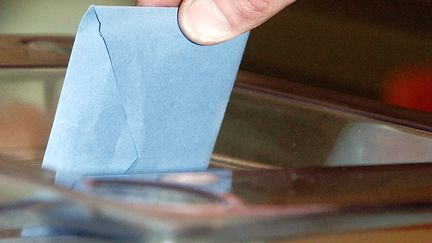 Une personne place son bulletin dans l'urne dans un bureau de vote de Saint-Denis lors des élections régionales de 2004. (JEAN AYISSI / AFP)