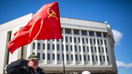 Un homme tient un drapeau sovi&eacute;tique devant le parlement de Crim&eacute;e, &agrave; Simferopol, le 17 mars 2014. (HANNIBAL HANSCHKE / DPA / AFP)