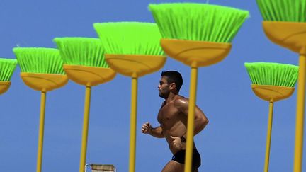 Un homme court pr&egrave;s d'une installation de balais plant&eacute;s en signe de protestation contre la corruption sur la plage de Copacabana (Br&eacute;sil), le 19 septembre 2011. (SERGIO MORAES / REUTERS)