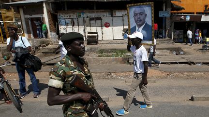 Un militaire patrouille alors qu'un partisan du pr&eacute;sident burundais Pierre Nkurunziza prom&egrave;ne son portrait, le 15 mai 2015, dans&nbsp;une rue de la capitale Bujumbura (Burundi). (GORAN TOMASEVIC / REUTERS)