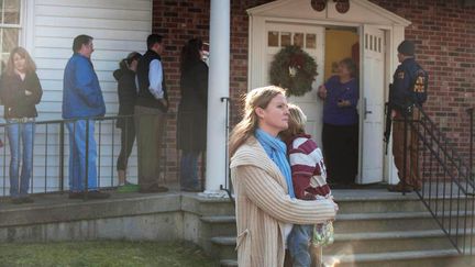 Une femme porte un enfant dans les bras devant la porte de l'&eacute;glise m&eacute;thodiste qui jouxte l'&eacute;cole &eacute;l&eacute;mentaire, vendredi 14 d&eacute;cembre 2012.&nbsp; (DOUGLAS HEALEY / GETTY IMAGES NORTH AMERICA)