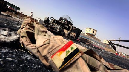 La veste d'un militaire irakien au sol, devant les restes carbonis&eacute;s d'un v&eacute;hicule de l'arm&eacute;e, &agrave; l'est de la ville de Mossoul (Irak), le 11 juin 2014. (SAFIN HAMED / AFP)