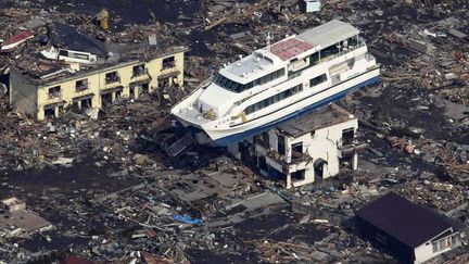 Une photo aérienne montre un bateau échoué sur le toit d'un immeuble au milieu d'une mer de débris dans la ville de Otsuchi, dans la prefecture d'Iwate, trois jours après les catastrophes naturelles qui ont endommagé la centrale nucléaire de Fukushima-Daiichi. «Le vendredi 11 mars 2011, à 5h46 TU (14h46 heure locale), un séisme de magnitude 9,0 se produit à 80 km à l’est de l’île d’Honshu au Japon», peut-on lire sur le site de l'Institut (français) de radioprotection et de sûreté nucléaire. «Ce séisme a généré un tsunami de grande ampleur» qui a conduit «à l'arrêt des quatre centrales nucléaires les plus proches de l’épicentre». «Le tsunami a entraîné la perte des systèmes de refroidissement des centrales de Fukushima Daiichi et Fukushima Daini, occasionnant un accident nucléaire avec relâchement de radioactivité.»

Ces catastrophes sont à l'origine de la mort de plus de 19.000 personnes, dont la majorité est morte noyée. En outre, indique Reuters, «plus de 160.000 personnes ont été évacuées des villes situées autour de la centrale et près de 10% d'entre elles vivent dans des logements temporaires disséminés dans la circonscription territoriale de Fukushima». De même, l'accident nucléaire de Fukushima pourrait provoquer «10.000 cancers de plus dans la population japonaise en raison des radiations, selon un rapport de deux ONG publié (mercredi 9 mars 2016) aux Etats-Unis», rapporte l'AFP.


	 


 


 .

 (YOMIURI SHIMBUN / AFP)