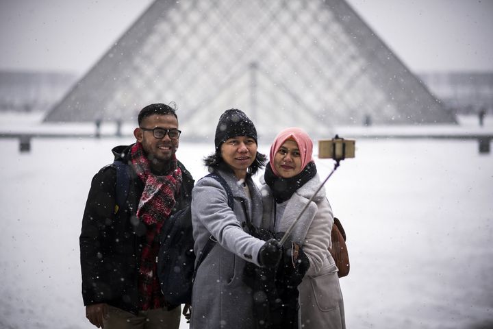 Des touristes se prennent en photo devant la pyramide du Louvre en février 2018.
 (LIONEL BONAVENTURE / AFP)