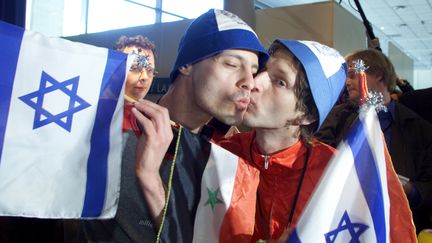 Les chanteurs Guy Assif et Roy Arad, membres du groupe "Ping Pong", représentant d'Israël au concours Eurovision, s'embrassent et tiennent des drapeaux israéliens et syriens, à Stockholm (Suède), le 12 mai 2000. (JONAS EKSTROMER / SCANPIX SWEDEN / AFP)