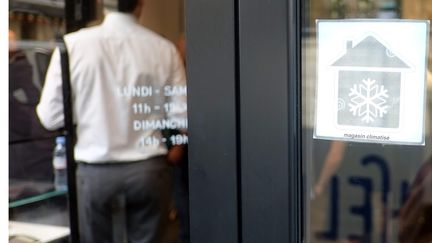 Une affichette "Magasin climatisé", sur la vitrine d'un établissement, le 26 juin 2019 à Paris. (BRUNO LEVESQUE / IP3 / MAXPPP)