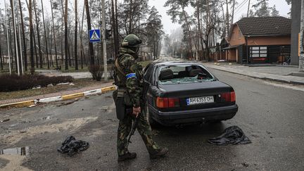 Un soldat ukrainien près d'une voiture&nbsp;endommagée à Irpin, près de Kiev (Ukraine), le 1er avril 2022. (METIN AKTAS / ANADOLU AGENCY / AFP)