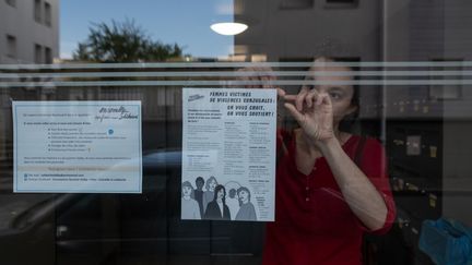 Une femme scotche une feuille de papier avec des informations et numéros d'urgence à destination des femmes victimes de violences conjugales dans le hall d'entrée d'un immeuble à Nantes, le 15 avril 2020. (JEREMIE LUSSEAU / HANS LUCAS / AFP)