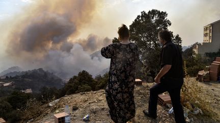 Un homme et une femme observent un incendie à proximité, dans les collines boisées&nbsp;de Kabylie&nbsp;(Algérie), le 11 août 2021. (RYAD KRAMDI / AFP)