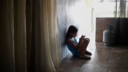 &nbsp;Une Vénézuélienne de sept ans, dont les parents ont émigré, utilise un téléphone portable dans sa maison du quartier de San Agustin à Caracas, le 5 août 2019. (FEDERICO PARRA / AFP)