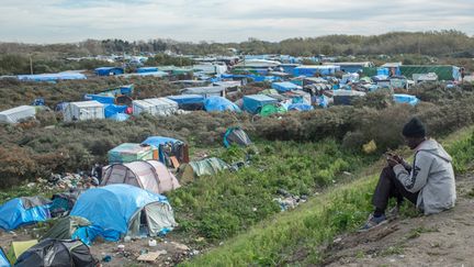 &nbsp; (Un migrant s’isole, le 31 octobre 2015, pour écouter de la musique avec en arrière-plan la "Jungle" de Calais © Maxppp)