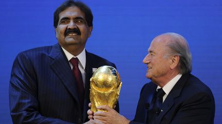 L'Emir du Qatar Sheikh Hamad bin Khalifa Al-Thani (à gauche) reçoit le trophée de la Coupe du monde des mains du président de la Fifa, Joseph Blatter (le 2 décembre 2010). (PHILIPPE DESMAZES / AFP)