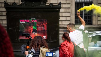 Un homme avec un fumigène jaune passe à côté de deux journalistes dans une manifestation sauvage de "gilets jaunes", samedi 10 septembre, à Paris. (XOSE BOUZAS / HANS LUCAS)