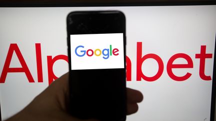 Le logo de Google s'affiche sur un téléphone portable placé devant le logo de la maison mère de l'entreprise, Alphabet, le 31 janvier 2019.&nbsp; (ALEXANDER POHL / NURPHOTO / AFP)