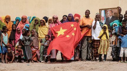 Le 4 juillet 2018 à Djibouti, sous le portrait du président Ismaël Omar Guelleh, la foule agite un drapeau chinois lors de&nbsp;la pose de la première pierre d'un complexe de 1 000 logements financé par la Chine. (YASUYOSHI CHIBA / AFP)