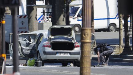 Un agent des forces de l'ordre se trouve à proximité de la voiture avec laquelle un homme a percuté un fourgon de gendarmerie, sur les Champs-Elysées, à Paris, le 19 juin 2017.  (THOMAS SAMSON / AFP)