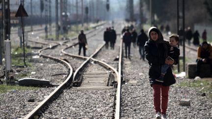 Une femme porte un enfant près du village d'Idomeni, à la frontière entre la Grèce et la Macédoine, mercredi 2 mars 2016. (SAKIS MITROLIDIS / AFP)