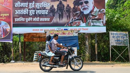 Un motard passe devant une affiche du Premier ministre Narendra Modi le 18 avril 2024 à Dantewada, en Inde.  (IDREES MOHAMMED / AFP)