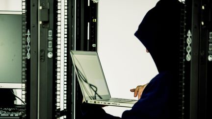 Un homme dissimulé par une cagoule lance une cyberattaque sur un réseau informatique. (RICHARD BRUNEL / MAXPPP)