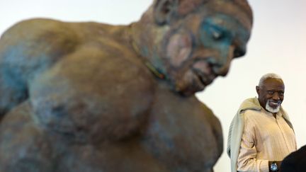 L'artiste sénégalais Ousmane Sow (à droite) devant l'une de ses statues représentant un guerrier nouba, le 15 juin 2013, lors d'une exposition à Besançon. L'œuvre illustre la couverture&nbsp;du livre "Atlas historique de l'Afrique - De la préhistoire à nos jours" (Autrement).&nbsp; (SEBASTIEN BOZON / AFP)