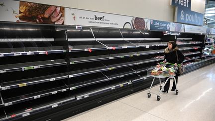 Une Britannique regarde les rayons vides dans un supermarché de Manchester, le 20 mars 2020. (OLI SCARFF / AFP)