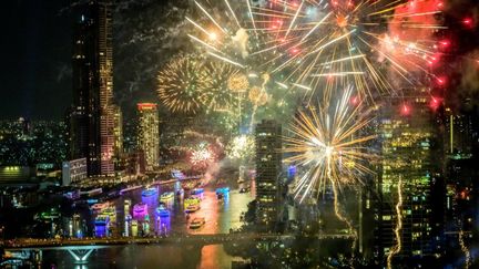 Le feu d'artifice à Bangkok, en Thaïlande, a dû rivaliser de couleurs face aux bateaux lumineux massés sur la rivière Chao Phraya. (MLADEN ANTONOV / AFP)