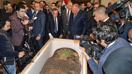 Le ministre égyptien des Affaires étrangères Sameh Choukri et  le directeur du Conseil suprême des Antiquités Mostafa Waziri, entourés de journalistes devant le sarcophage restitué par les Etats-Unis, le 2 janvier 2023 au Caire (Egypte). (AFP)