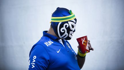 Un supporter br&eacute;silien tente de boire une bi&egrave;re &agrave; travers son masque, avant le match contre la Croatie, le 12 juin. (BEHROUZ MEHRI / AFP)