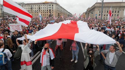 Des manifestants portent un drapeau de la contestation en Biélorussie, à Minsk, le 23 août 2020. (VASILY FEDOSENKO / REUTERS)