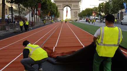 Des techniciens installent une p&icirc;ste d'athl&eacute;tisme sur les Champs Elys&eacute;es pour f&ecirc;ter la candidature de Paris le 4 juin 2005. (ERIC FEFERBERG / AFP)