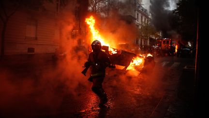 Un pompier devant une voiture incendiée lors de la manifestation des "gilets jaunes" à Paris, le 1er décembre 2018. (ABDULMONAM EASSA / AFP)