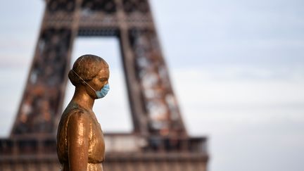 Une statue de bronze porte un masque devant la tour Eiffel, à Paris. (ALAIN JOCARD / AFP)