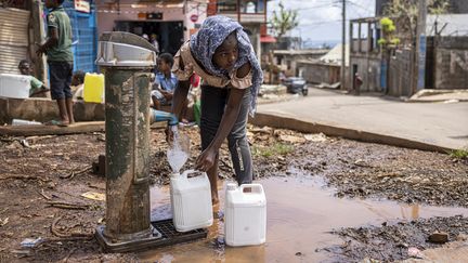 Une jeune fille rempli des bidons d'eau à Koungou, sur l'île de Mayotte, le 27 décembre 2024. (PATRICK MEINHARDT / AFP)