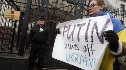 Une manifestante brandit une pancarte indiquant "Poutine, &ocirc;te tes mains de l'Ukraine", devant l'ambassade russe &agrave; Kiev, le 1er mars 2014. (YURY KIRNICHNY / AFP)