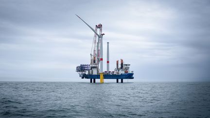 Un navire&nbsp;assemble la première éolienne offshore française dans un parc éolien, au large de Saint-Nazaire (Loire-Atlantique), le 12 avril 2022. (SEBASTIEN SALOM-GOMIS / AFP)