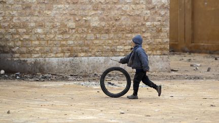 Un enfant joue avec une roue, le 28 décembre 2016, dans le village rebelle Tal Aar, dans la province d'Alep (Syrie). (KHALIL ASHAWI / REUTERS)