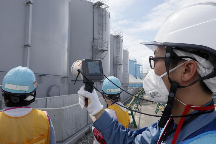 Un employé de Tepco mesurant la radioactivité devant des citernes contenant de l'eau contaminée par des éléments radioactifs,&nbsp;le&nbsp;27 juillet 2018, sur le site de la centrale nucléaire accidentée de Fukushima (Japon). (KIMIMASA MAYAMA / AFP)