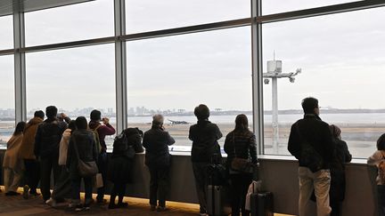 Des passagers observent les restes d'un avion de la Japan Airlines qui a brûlé après une collision avec un autre appareil, le 3 janvier 2024, à l'aéroport de Tokyo-Haneda (Japon). (DAVID MAREUIL / ANADOLU / AFP)