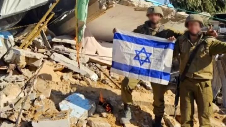 Des soldats israéliens posent au milieu de ruines à Gaza avec le drapeau national, avec derrière eux un drapeau palestinien brûlé. (X / YOUNIS TIRAWI)