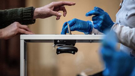 Un citoyen dépose son enveloppe dans l'urne avec les précautions d'usage liées au coronavirus, le 15 mars 2020 à Lyon. Photo d'illustration. (JEFF PACHOUD / AFP)